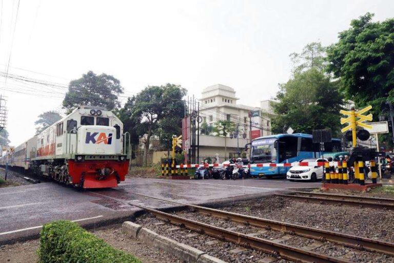 Locomotive approaching a crossing with parked buses and cars nearby at a railway intersection.