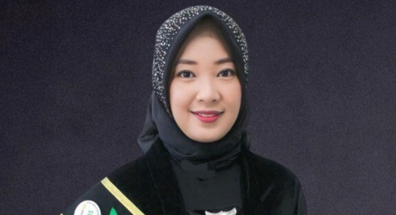 Portrait of a woman wearing a black hijab and an award sash, smiling against a dark backdrop.