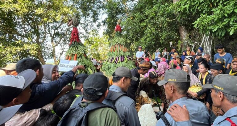 Crowd of people at an outdoor festival gathered around two tall towers made of leaves and vegetables.
