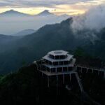 Tiered wooden viewing platform on a foggy mountain slope at dawn, with distant volcano silhouettes still visible above the haze.