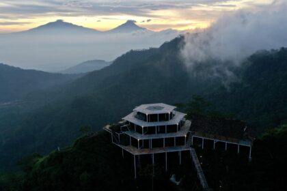 Tiered wooden viewing platform on a foggy mountain slope at dawn, with distant volcano silhouettes still visible above the haze.