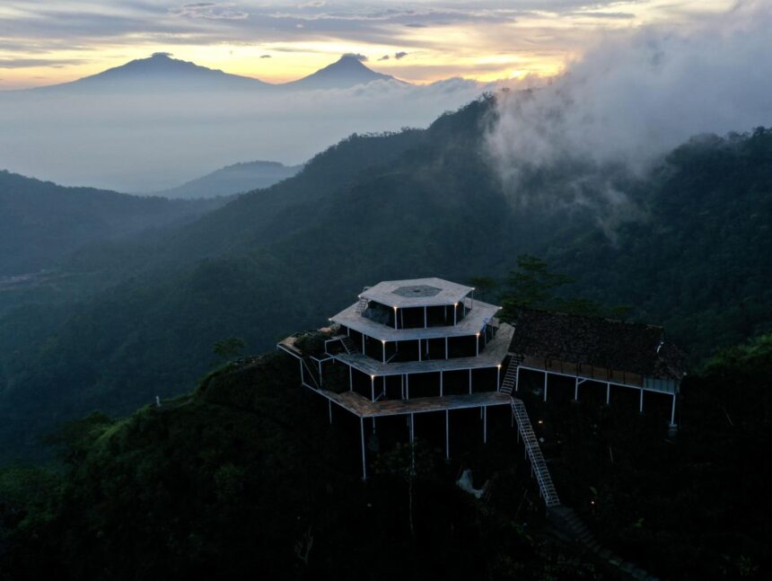 Tiered wooden viewing platform on a foggy mountain slope at dawn, with distant volcano silhouettes still visible above the haze.