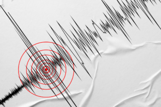 Seismograph recording with jagged black lines and red concentric circles marking a tremor focus on crumpled paper.