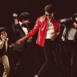 Four performers in Michael Jackson costumes pose and dance on a dark stage, iconic outfits and moves shared together.