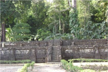 Stone step stairway flanked by low walls in a tropical garden or ruin setting, with dense jungle behind.