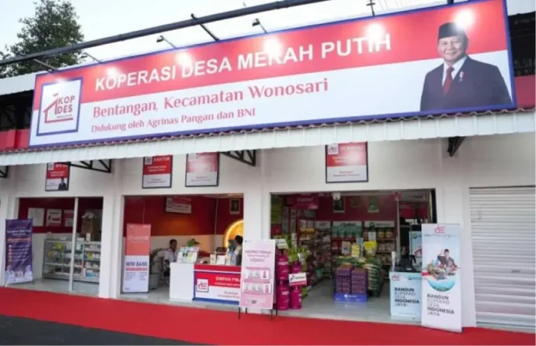 A bright storefront of Koperasi Desa Merah Putih with a large red banner and a portrait on the right, showcasing shelves and products inside the cooperative store.