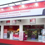 Front view of Koperasi Desa Merah Putih store with a red sign, open entrance, and customers shopping inside.