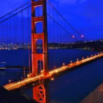 Golden Gate Bridge lit in orange at night, spanning San Francisco Bay with the city lights in the distance.