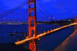 Golden Gate Bridge lit in orange at night, spanning San Francisco Bay with the city lights in the distance.