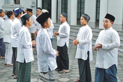 Group of men in white traditional tunics and caps standing in a line outside a building courtyard, chatting.
