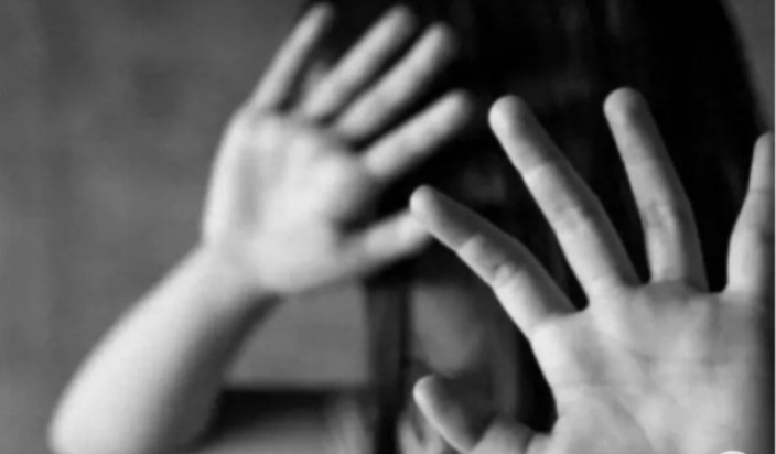 Black-and-white photo of a person raising their hands to shield their face, conveying distress or fear.