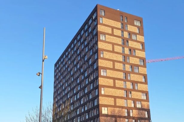 Tall brick apartment building with many windows in a city plaza, bike resting on a rack, and an Erasmus Plaza map sign in the foreground.
