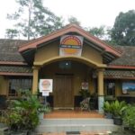 Front view of a small museum building with yellow walls, red-tiled roof, and a circular sign above the entrance.