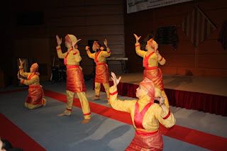 Dancers in red and yellow traditional costumes performing a synchronized routine on a gym stage.