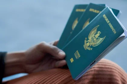 Blue Indonesian passport held in a hand, showing the crest on the cover against a blurred background