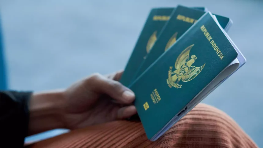 Blue Indonesian passport held in a hand, showing the crest on the cover against a blurred background
