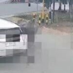 White SUV parked on a street next to a curb, with another car visible on the right; appears to be a CCTV frame with pixelated artifacts across the image.