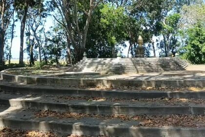 Circular stone amphitheater-like steps leading up to a small monument statue among trees in a park setting