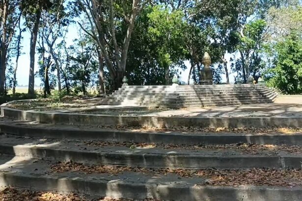 Circular stone amphitheater-like steps leading up to a small monument statue among trees in a park setting