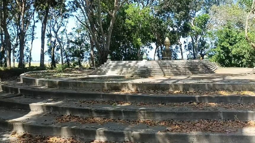 Circular stone amphitheater-like steps leading up to a small monument statue among trees in a park setting