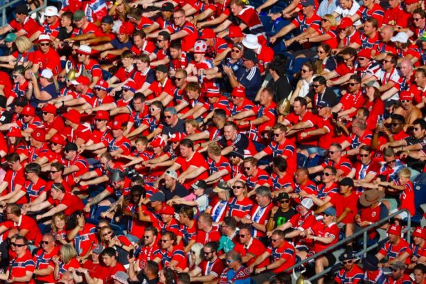 Large crowd of sports fans in red, seated in stadium stands and cheering at a game.
