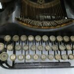 Front view of a vintage manual typewriter with cream circular keys and visible typebars, showing the keyboard and rusted metal frame.