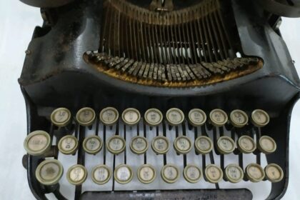Front view of a vintage manual typewriter with cream circular keys and visible typebars, showing the keyboard and rusted metal frame.