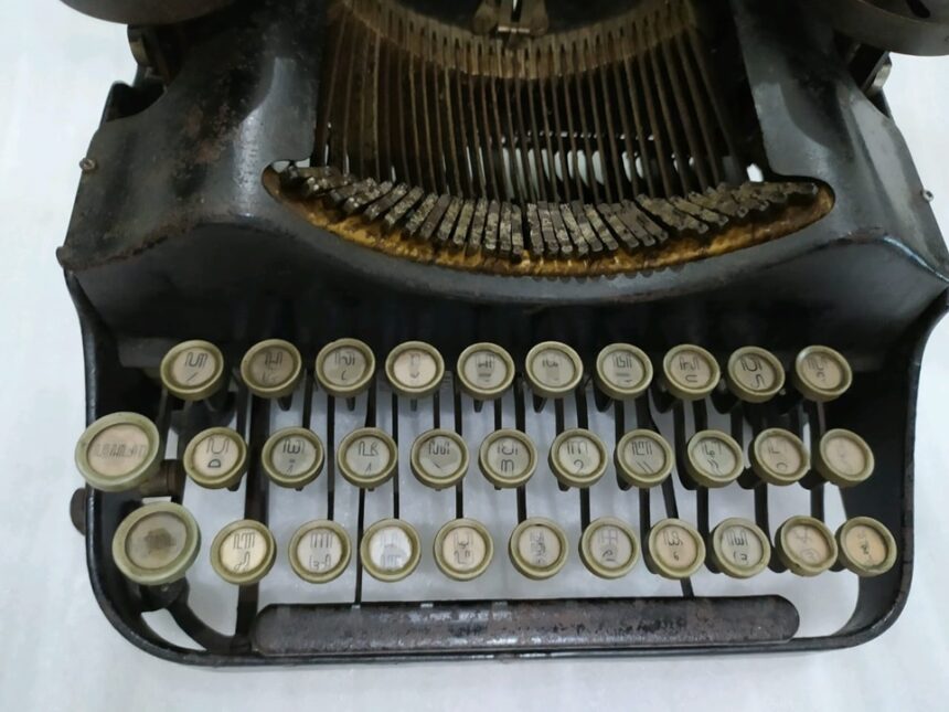 Front view of a vintage manual typewriter with cream circular keys and visible typebars, showing the keyboard and rusted metal frame.
