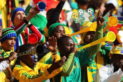 Energetic South African soccer fans in green and yellow cheer, blowing vuvuzelas.