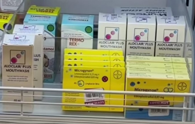 Shelf of pharmaceutical boxes on a store shelf, including Aloclar Plus Mouthwash (white boxes), blue Termorex/Relco items, and bright yellow Microgynon boxes, suggesting a pharmacy display.