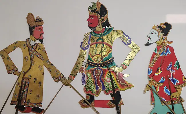 Three ornate warrior figures in colorful traditional robes, standing with swords, mid-heroic scene.