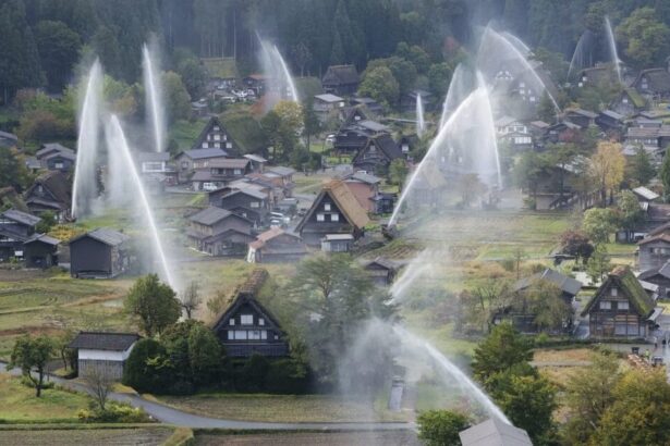Aerial view of a rural village with steep thatched-roof houses as large water sprinklers arc over the scene, spraying fountains across the landscape.
