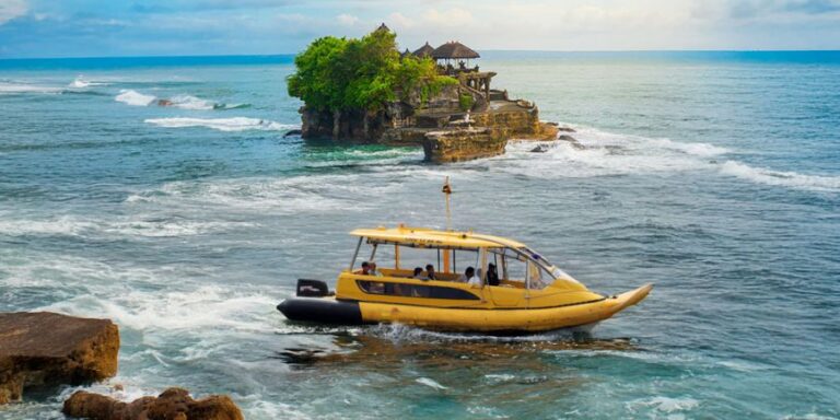 Yellow passenger boat glides near a rocky island with green trees and a thatched pavilion on top, in blue ocean.