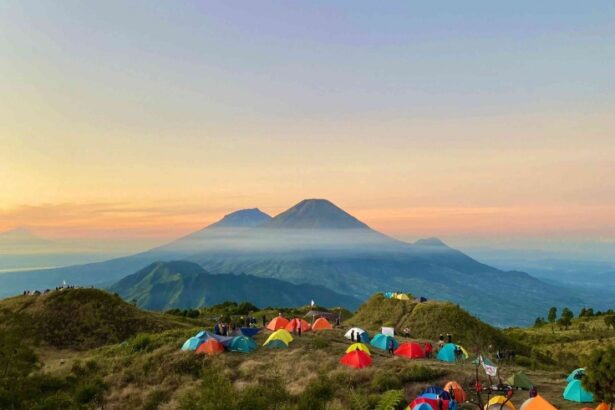 Colorful tents scattered on a grassy hillside at sunset with misty mountains in the distance