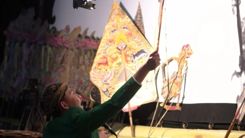 Performer in a green outfit reaches toward colorful, triangular props on stage during a traditional performance.