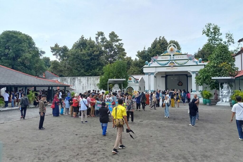 Crowded temple courtyard with visitors gathering near a decorated white temple building on a sunny day.