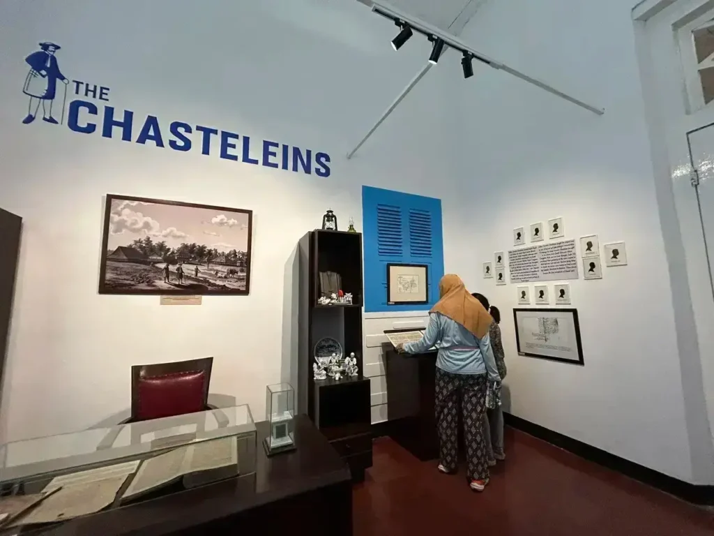 Museum exhibit titled 'THE CHASTELEINS' with two visitors examining a display case and wall-mounted photos/frames around them.