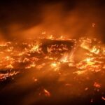 Nighttime wildfire burning through dry vegetation with bright flames and rising smoke across a scorched landscape