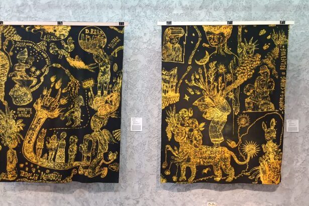 Two black-and-gold tapestries with intricate yellow drawings hanging on a gallery wall, each with a small placard beside it.