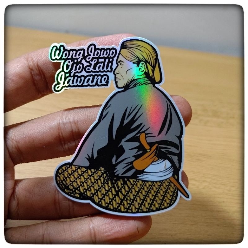Sticker showing a man seated with his back turned, wearing a gray shirt and patterned pants, with a knife at his belt and stylized text in the corner.