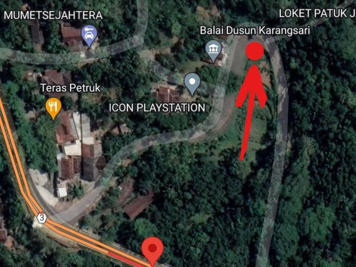 Satellite map of a forested area showing roads, with a red location pin low-left and a red arrow pointing to a spot near Balai Dusun Karangsari and ICON PLAYSTATION.