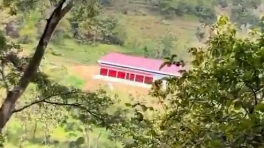 ygiluilgu - Mabur.co Red-roofed, single-story building with a row of openings in a green hillside, viewed through trees.