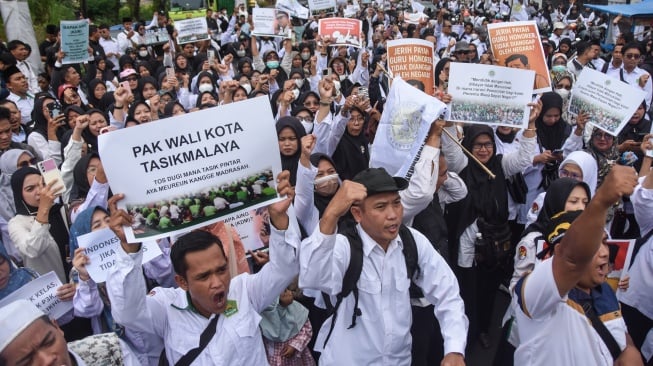 Large crowd of protesters marching in white clothing, holding placards including 'PAK WALI KOTA TASIKMALAYA'