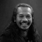 Portrait of a man with long hair and a mustache, smiling broadly at the camera.