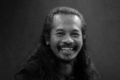 Portrait of a man with long hair and a mustache, smiling broadly at the camera.