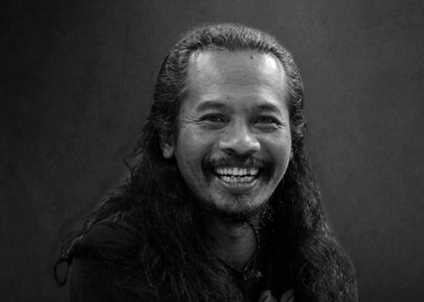 Portrait of a man with long hair and a mustache, smiling broadly at the camera.