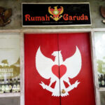 Double red doors with a white Garuda figure forming a heart, above a sign that reads 'Rumah Garuda'