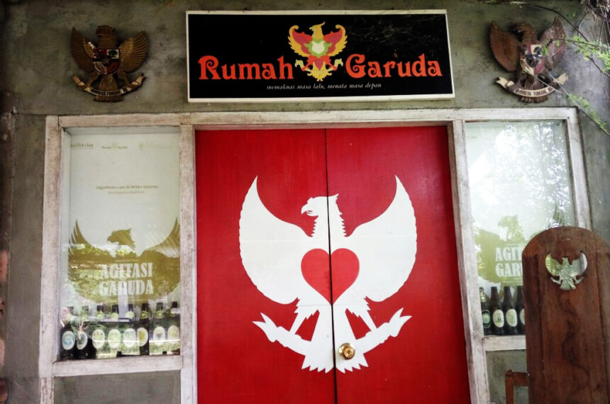 yuhol - Mabur.co Double red doors with a white Garuda figure forming a heart, above a sign that reads 'Rumah Garuda'