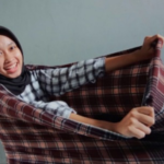 Smiling woman wearing a hijab pulls a plaid blanket toward the camera.