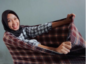 Smiling woman wearing a hijab pulls a plaid blanket toward the camera.